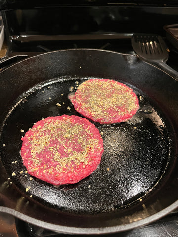 Frozen burger patties in a pan with seasoning