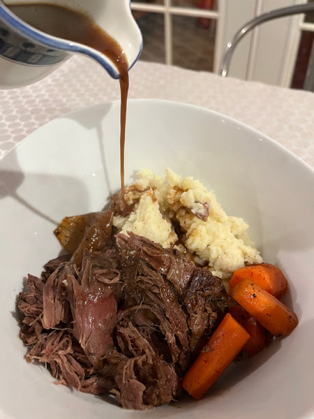 Gravy pouring onto a roast with potatoes and carrots