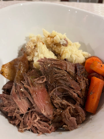 A portion of elk chuck roast in a bowl with potatoes and carrots