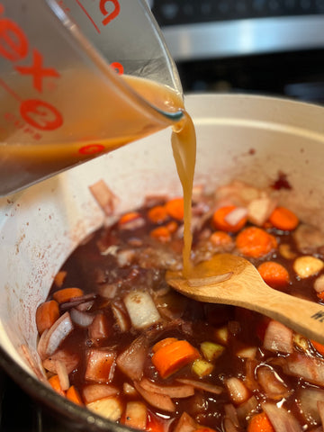 Broth pouring into a pot of vegetables