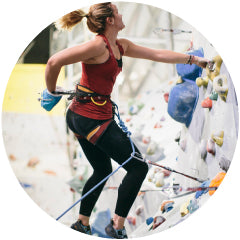 Frau mit Seilen in Kletterhalle an der Kletterwand befestigt.