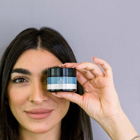 Woman holding beauty by earth hyaluronic acid night cream over her eye