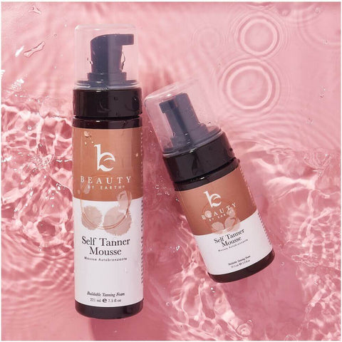 2 bottles of beauty by earth self tanning mousse on a pink background