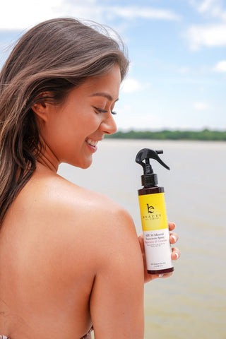 Girl holding beauty by earth's spray sunscreen in the peppermint & geranium scent