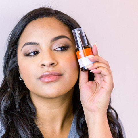 Image of a woman holding the BBE Vitamin C serum up to her cheek.