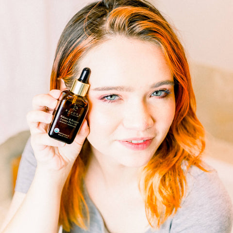 Girl holding up beauty by earth's balance & restore facial oil