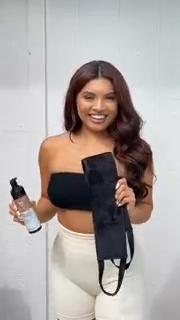 A smiling woman holding a spray bottle and a black article of clothing.