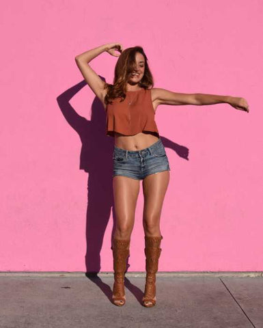 A tan girl posing in front of a pink wall
