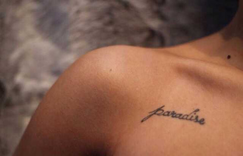 Up close shot of a woman's tan shoulder with a paradise tattoo
