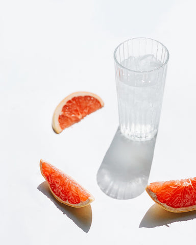 grapefruit slices surrounding a glass of water on a white background