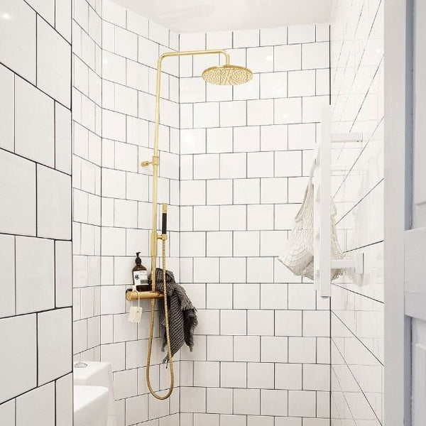 Image of a golden shower head in a white tiled bathroom.