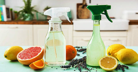 Image of two natural cleaning products on a countertop, with citrus fruits surrounding the bottles.