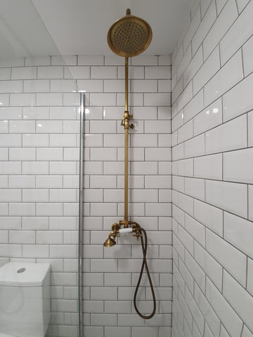 Image of a white tiled shower with a golden faucet head
