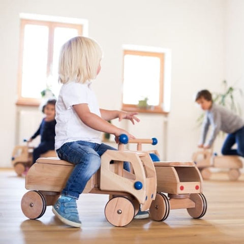 Kinder fahren mit Holz Rutschfahrzeugen Fred durch Wohnzimmer
