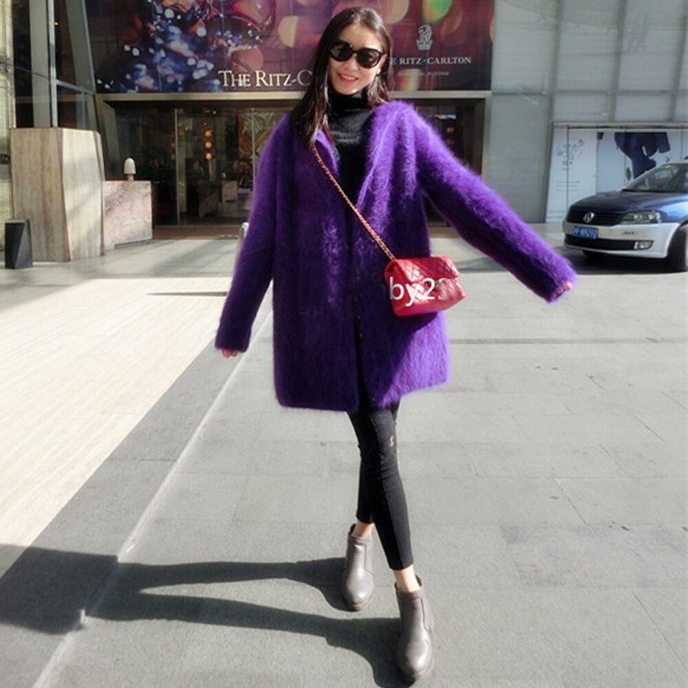 Woman wearing purple coat and blue jeans black sunglasses and red bag