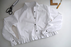 Collared blouse with frilled edging at waist and at cuffs, displayed flat on table