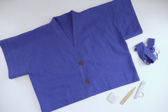 A cropped linen shirt laid out on table with small pile of thread ends and sewing tools