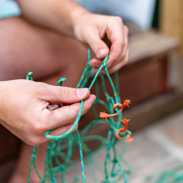 A pair of hands untangling a green and orange fishing net