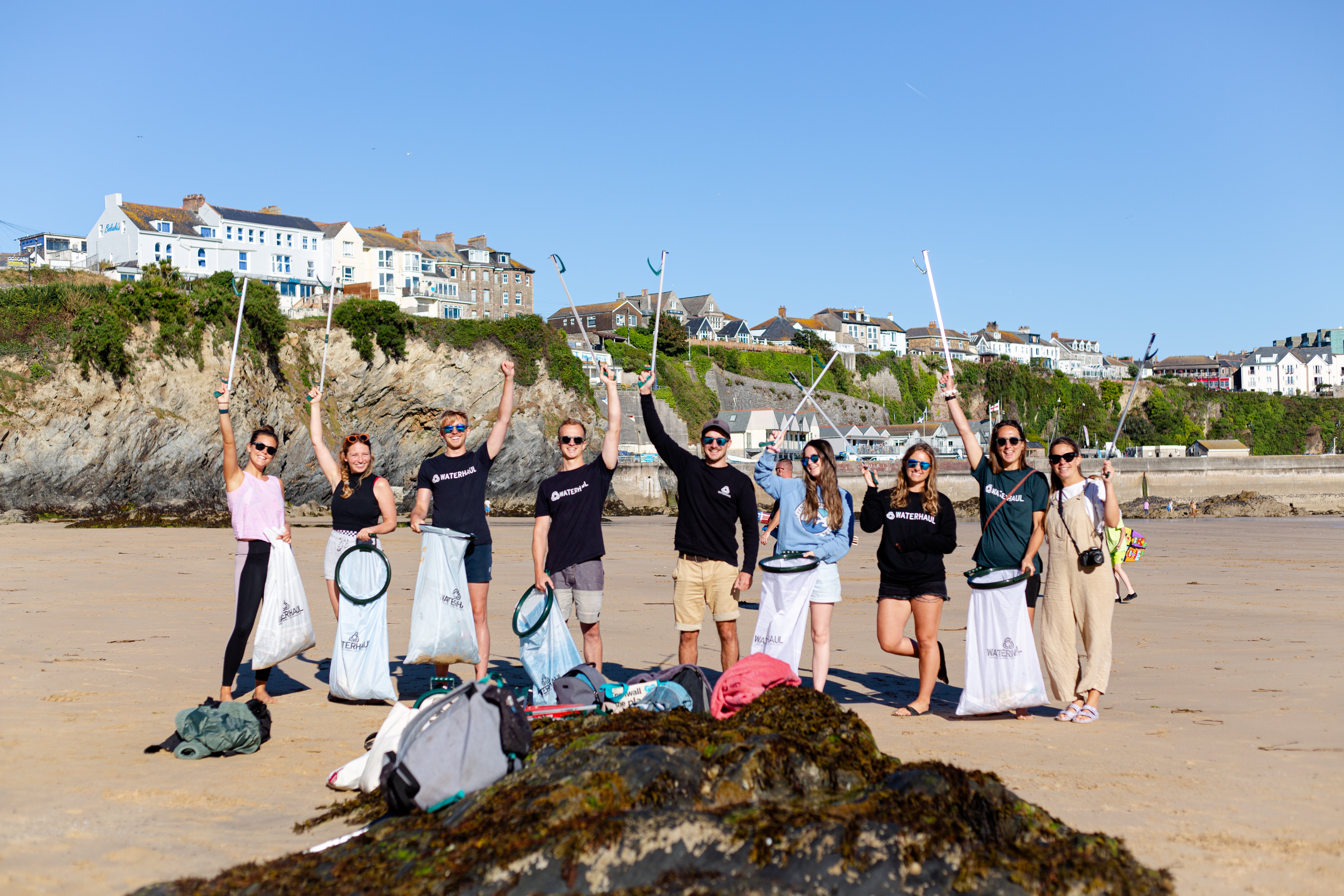 A group of people on a beach holding litter picking equipment