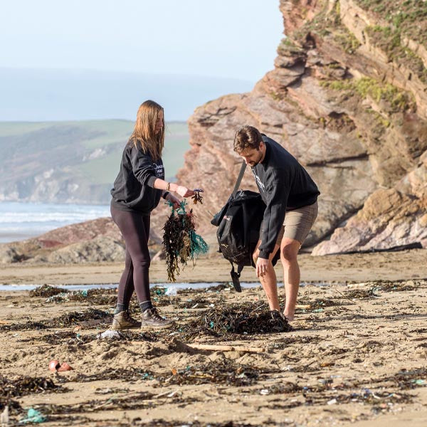 Two people collecting washed up fishing gear amongst seaweed on a beach in Cornwall