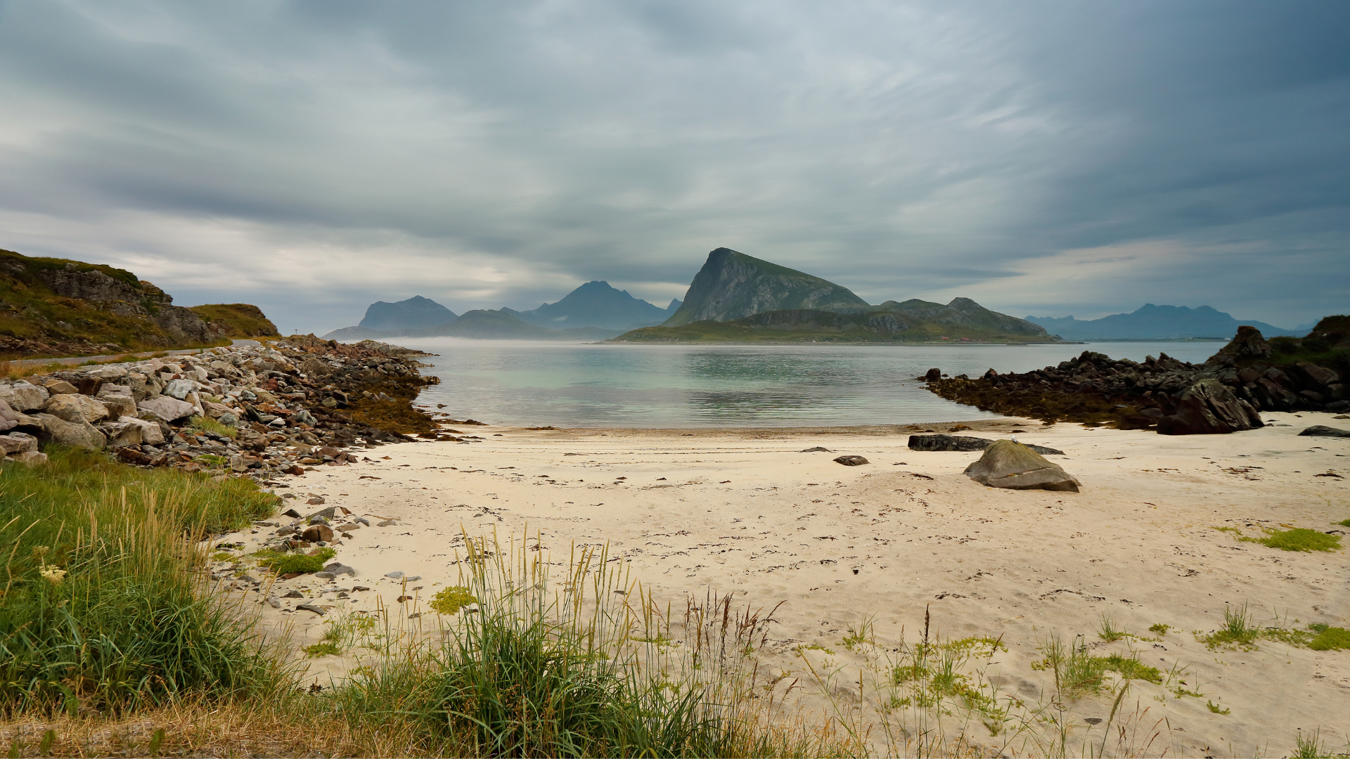 A sandy beach in norway with mountains in the distance