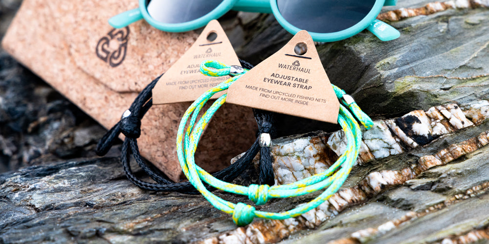 Green and black eyewear straps with craft paper tags on rock, with sunglases and a cork case in the background