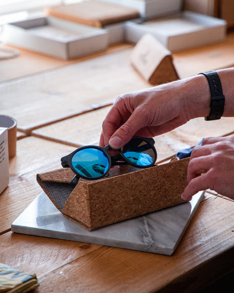 A pair of Waterhaul sunglasses being put into a folding cork glasses case