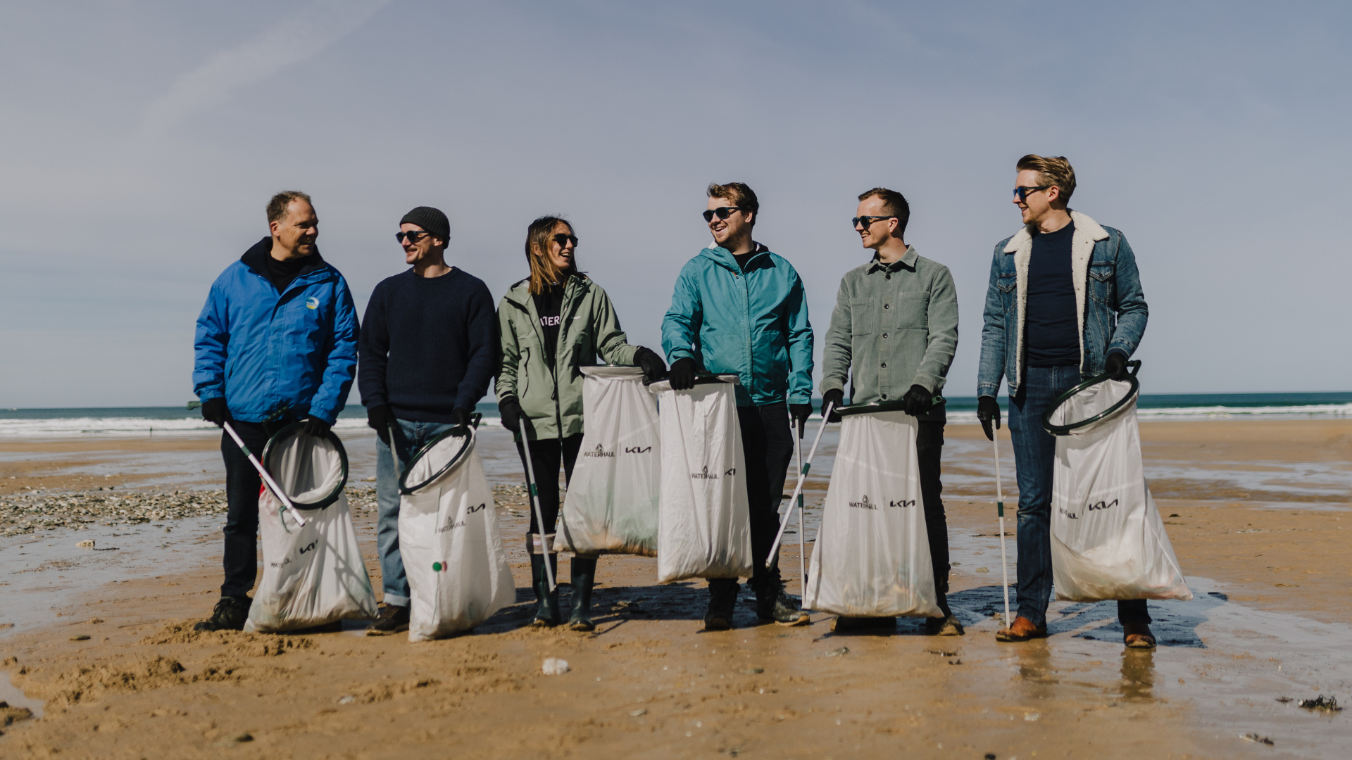 A group of people on a beach with litter picking equipment