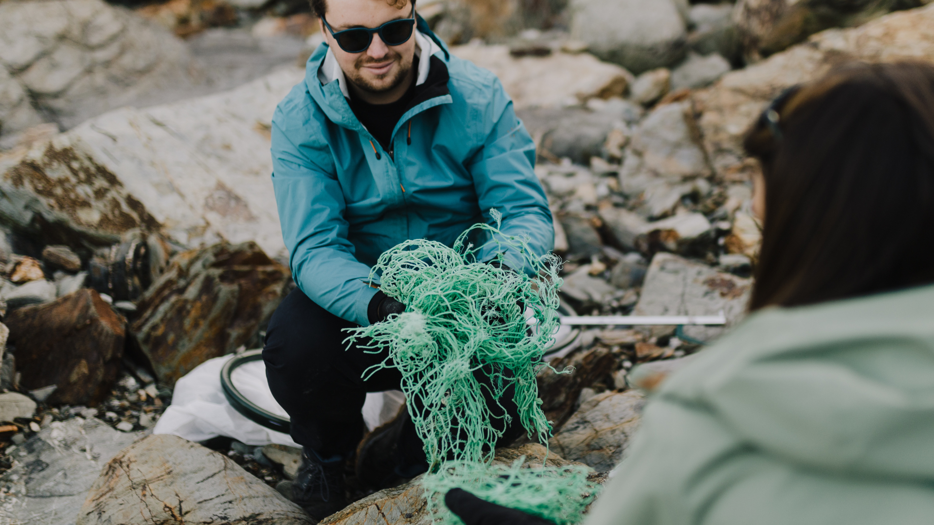 A person holding a ghost fishing net on a rocky landscape.