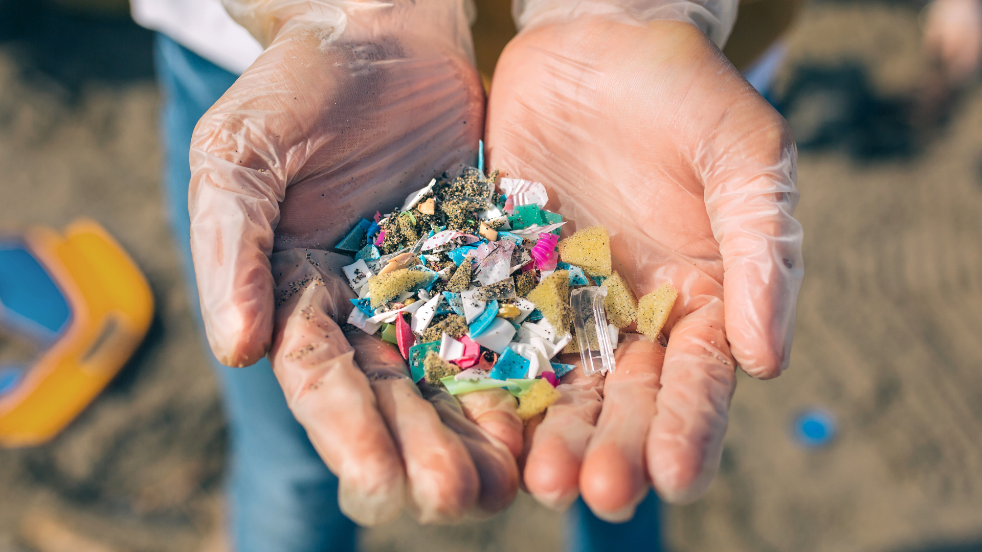 A pair of cupped hands wearing clear gloves holding colourful pieces of plastic.