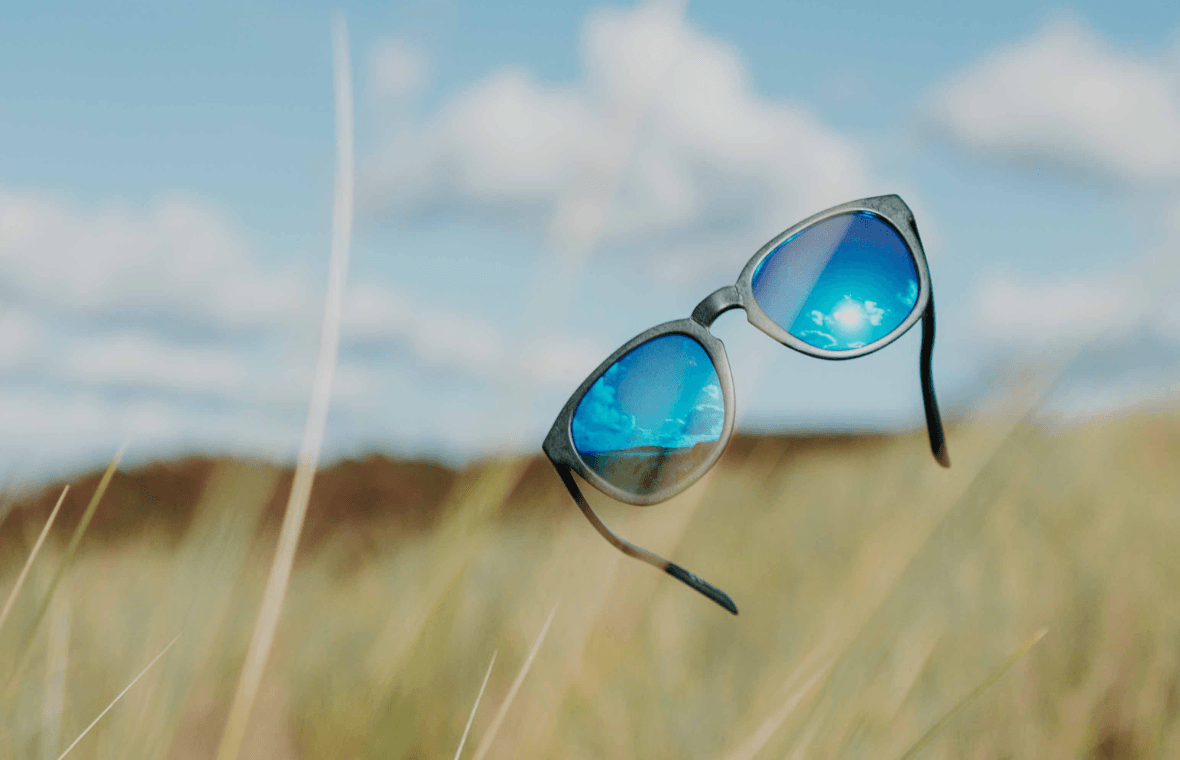 Pair of sunglasses with reflective blue lenses thrown into air above grassy sand dunes