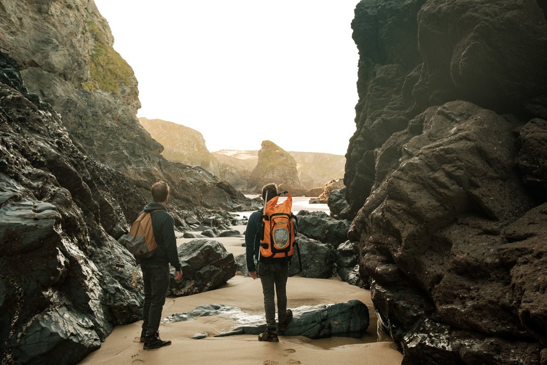 two people with bright orange backpacks looking at rocky beach