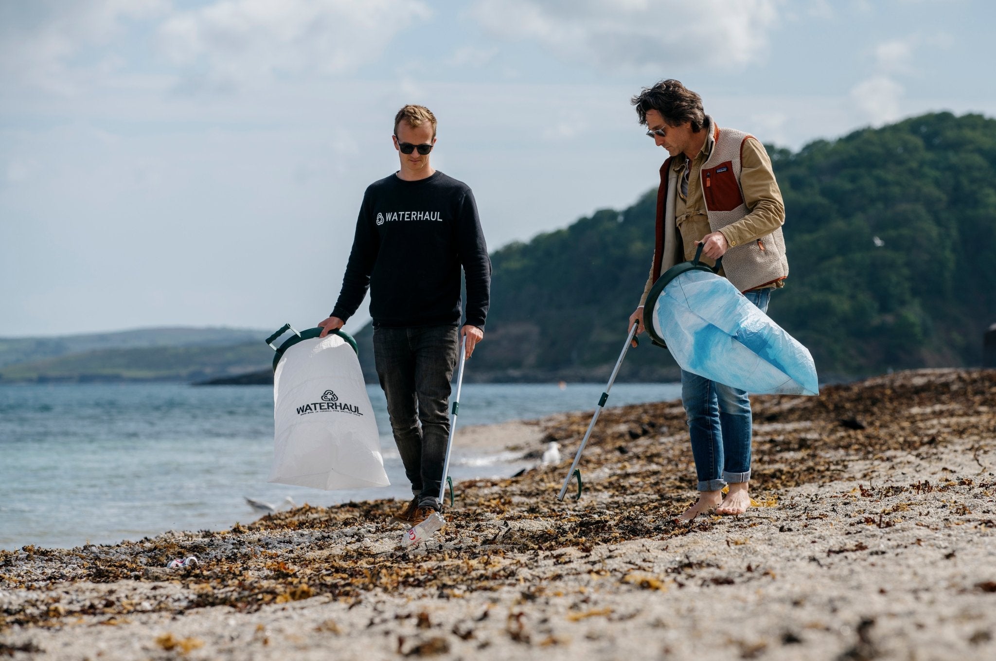 two people collecting litter on a beach covered with seaweed and plastic waste