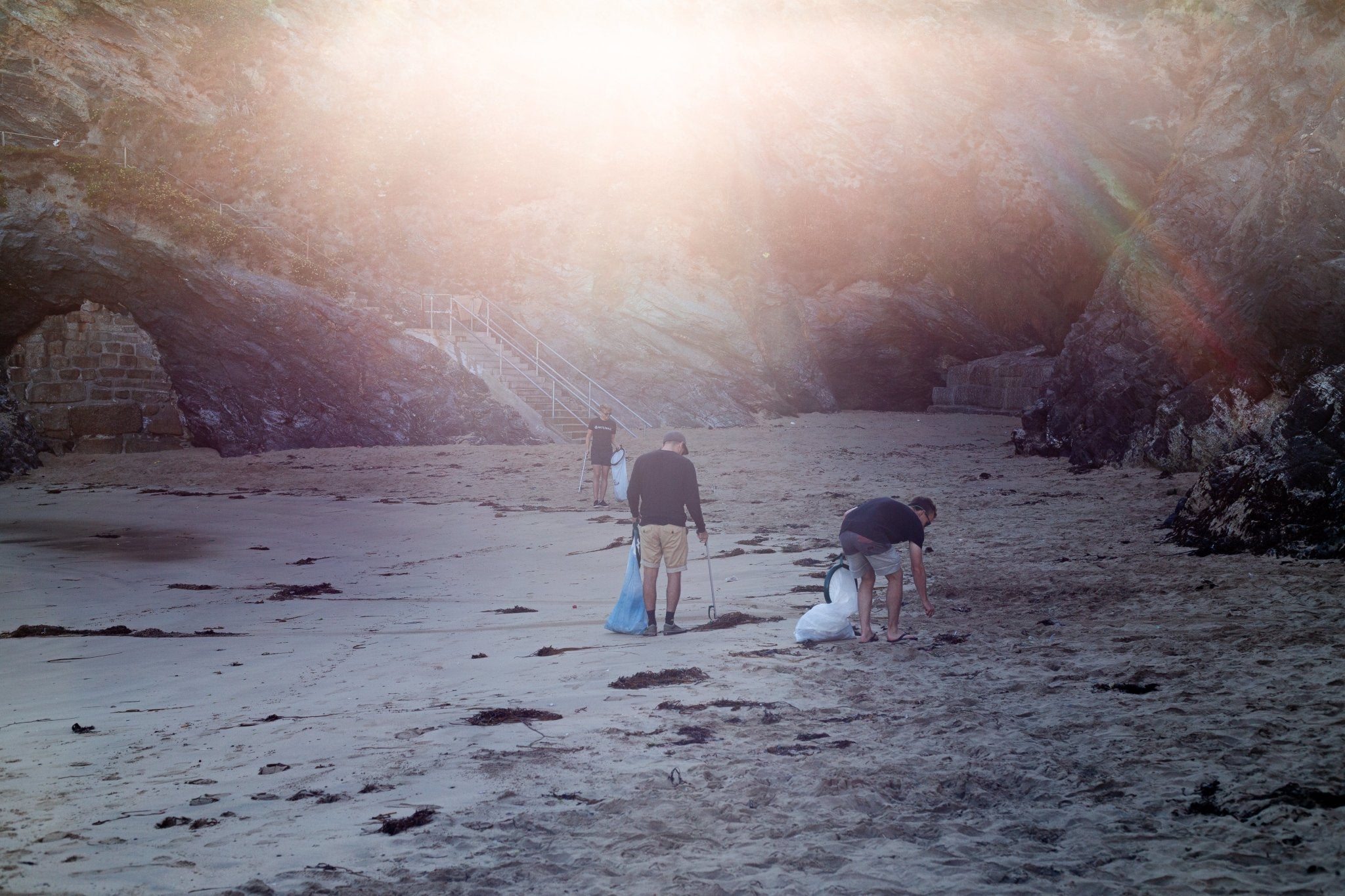 People collecting litter on a beach below cliffs