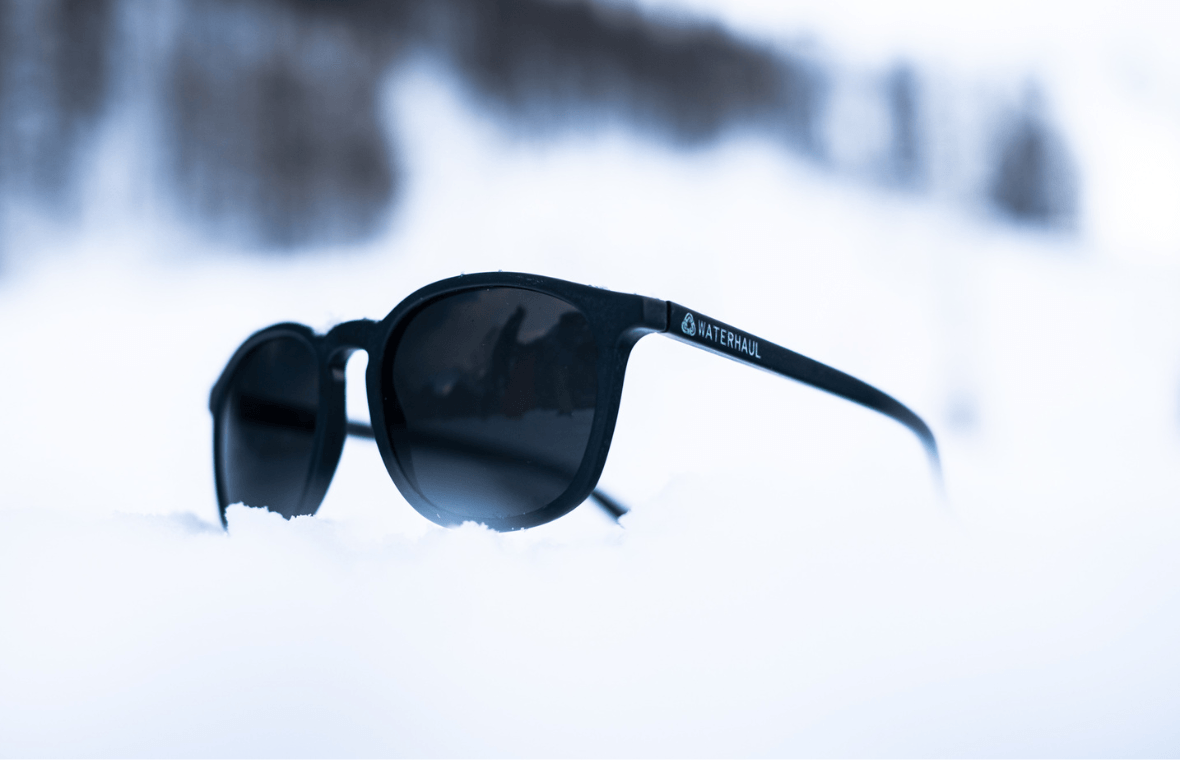 pair of black sunglasses in snow with snow covered trees in the background