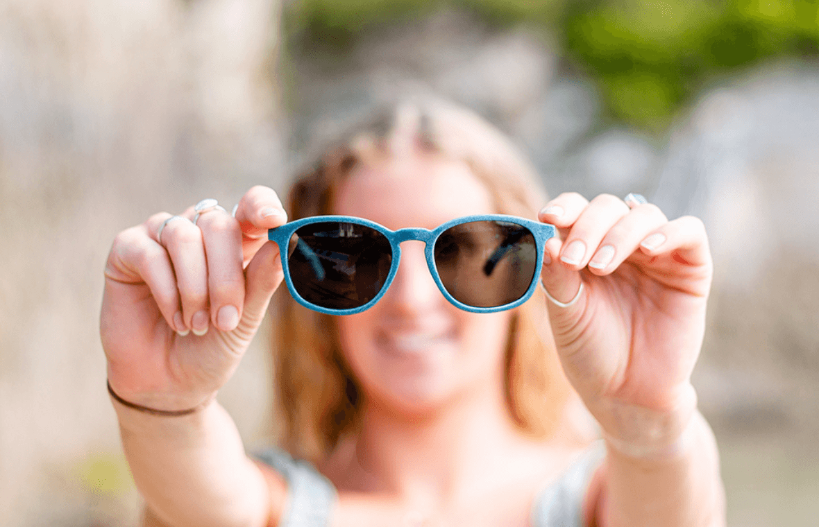 girl holding blue sunglasses out in front of her face. 