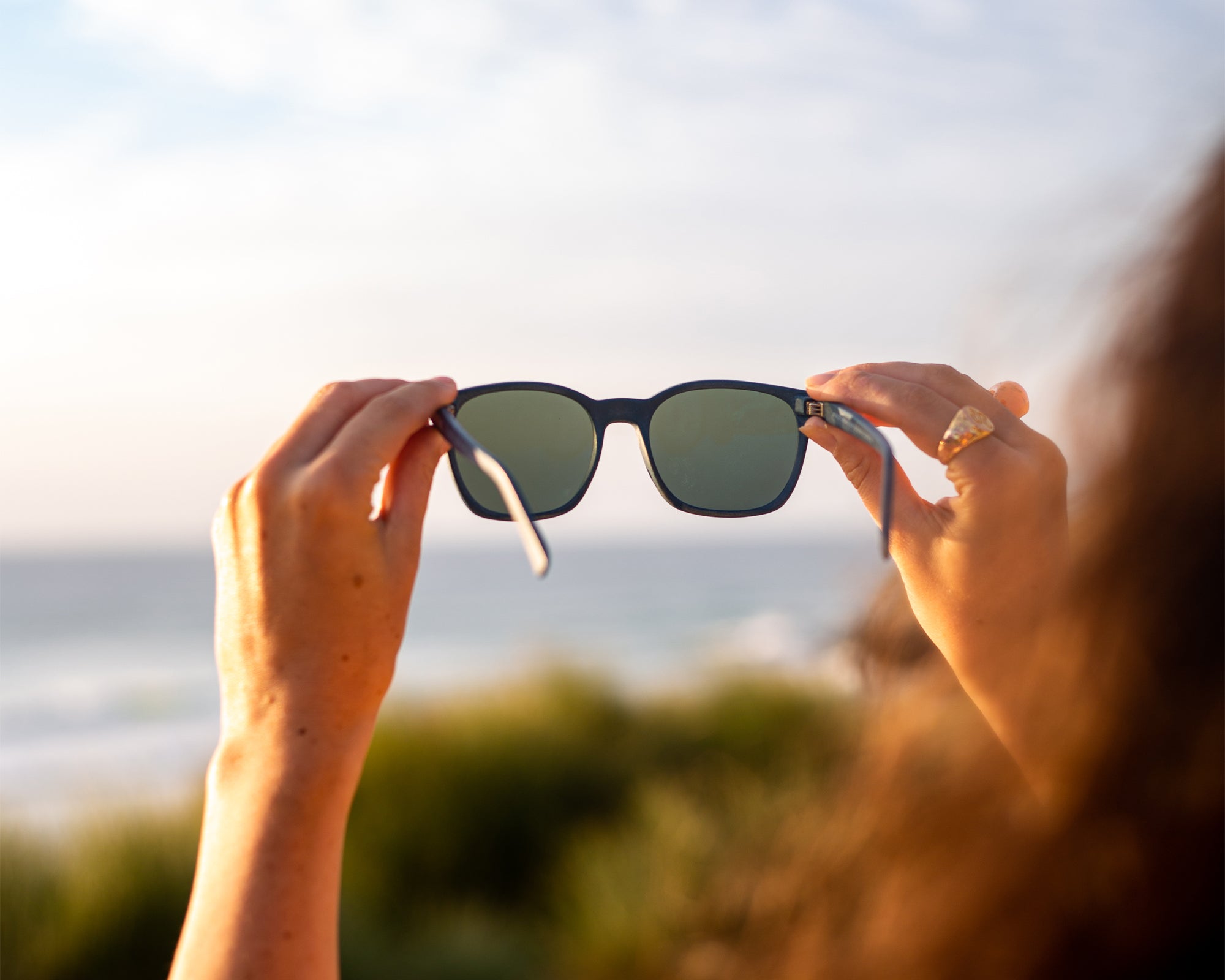 female model holding waterhaul fitzroy navy sunglasses against sky