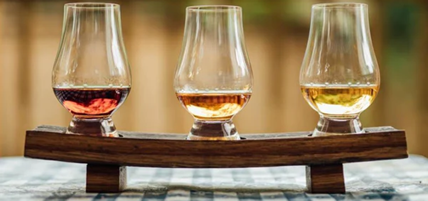 three glasses with different whiskies in them on a tray. the tray is on a checkered table cloth