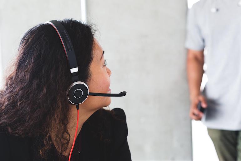 App store lessons: Photo of a woman wearing a customer service headset turning her head to speak to a colleague across the room.