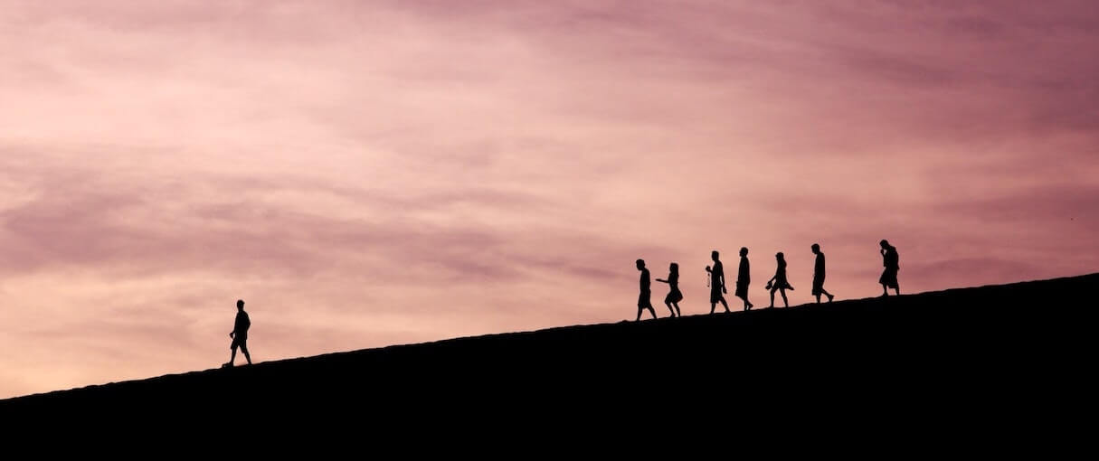 Development trends 2023: Wide shot photograph of a person leading a group on a hillside hike at dawn