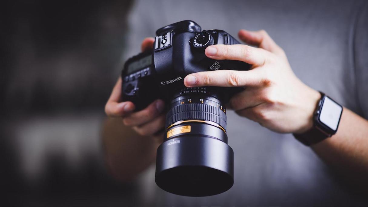 A mid-range photograph of a professional photographer holding a Canon DSLR camera