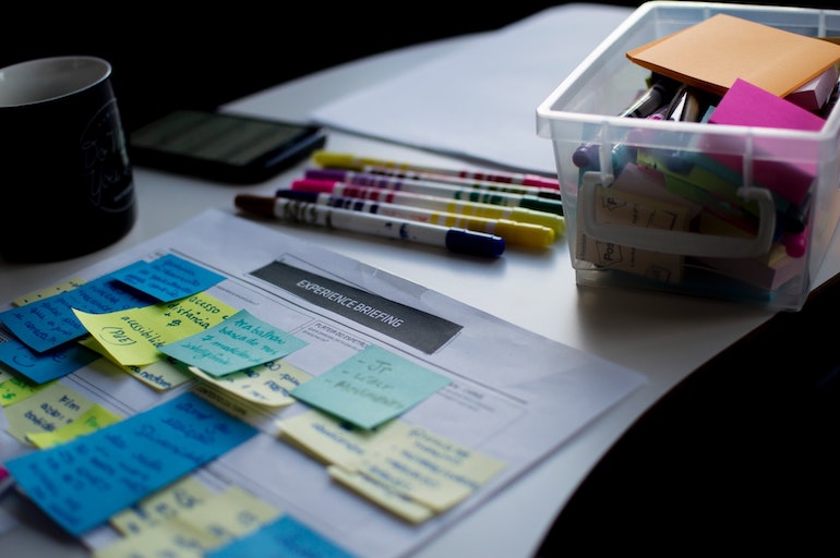 Reply to reviews: A large strategy sheet is covered with colourful post-it notes on a table with a small, clear bucket of markers next to it.