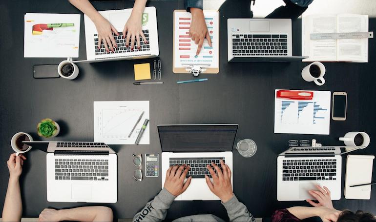 theme store success: An overhead image of a desk with a team of people working on Macbook laptops.