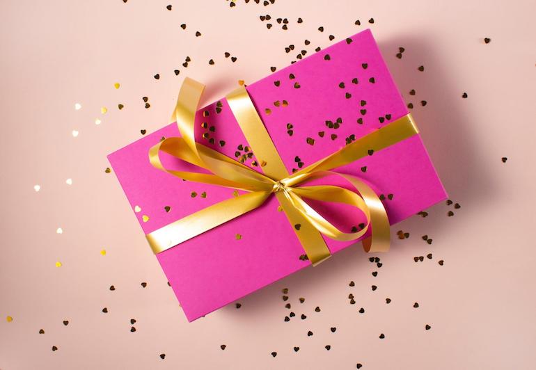 unboxing: pink package wrapped in gold, sprinkled with glitter, against a pale pink backdrop