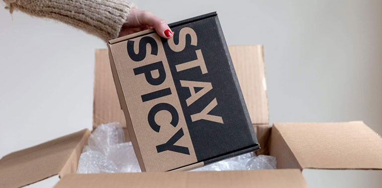 unboxing: hand pulling a box out of a package, the box says 'stay spicy'