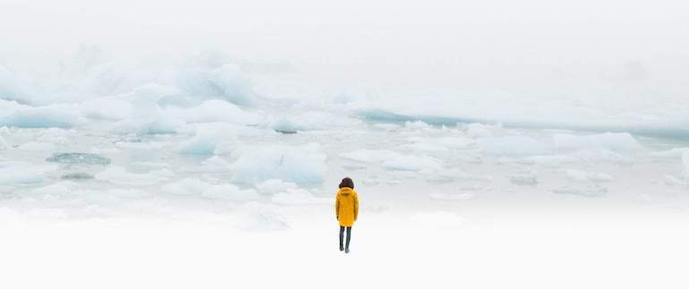 what is impostor syndrome: person standing on white glacier with yellow jacket