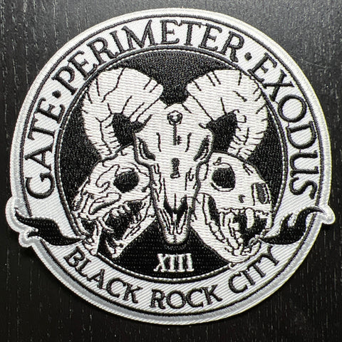 photo of a black and white patch featuring three skulls, flames, and the words "gate, perimeter, exodus; black rock city"