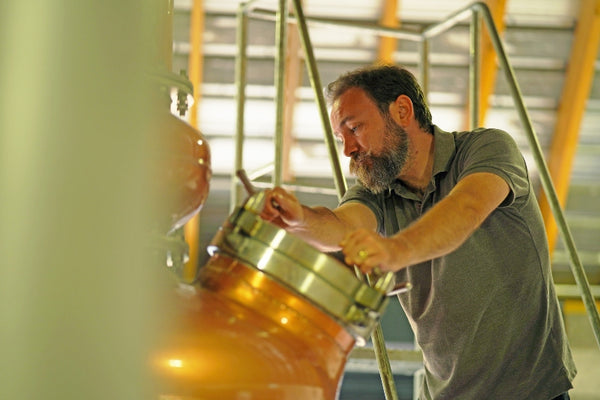 Darnley's Gin Distiller Scott Gowans checks the gin still before beginning the run. Scott is wearing a grey polo shirt on the right hand side of the image, with the hatch of the gin still in the centre. The gin still is made of copper.