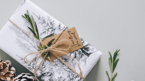 Christmas wrapping paper and a gift tag saying “something you need” finished with a sprig of rosemary