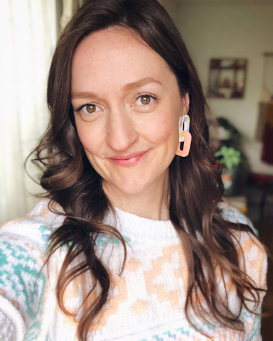 Becca Hildebrand, maker and owner of Hildesign, wearing a pair of the NEXA earrings and wearing a pastel sweater